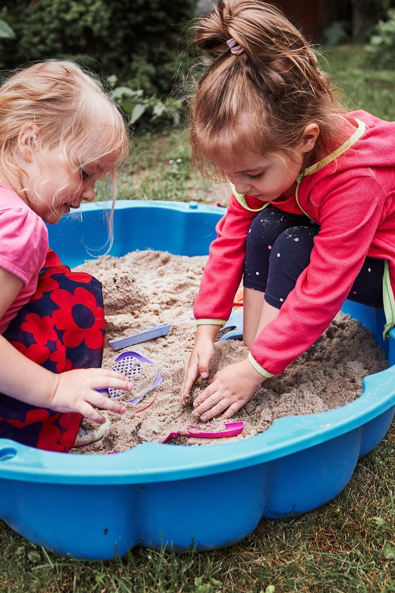 Children, little girls, playing in sandbox in playground outside on summer day