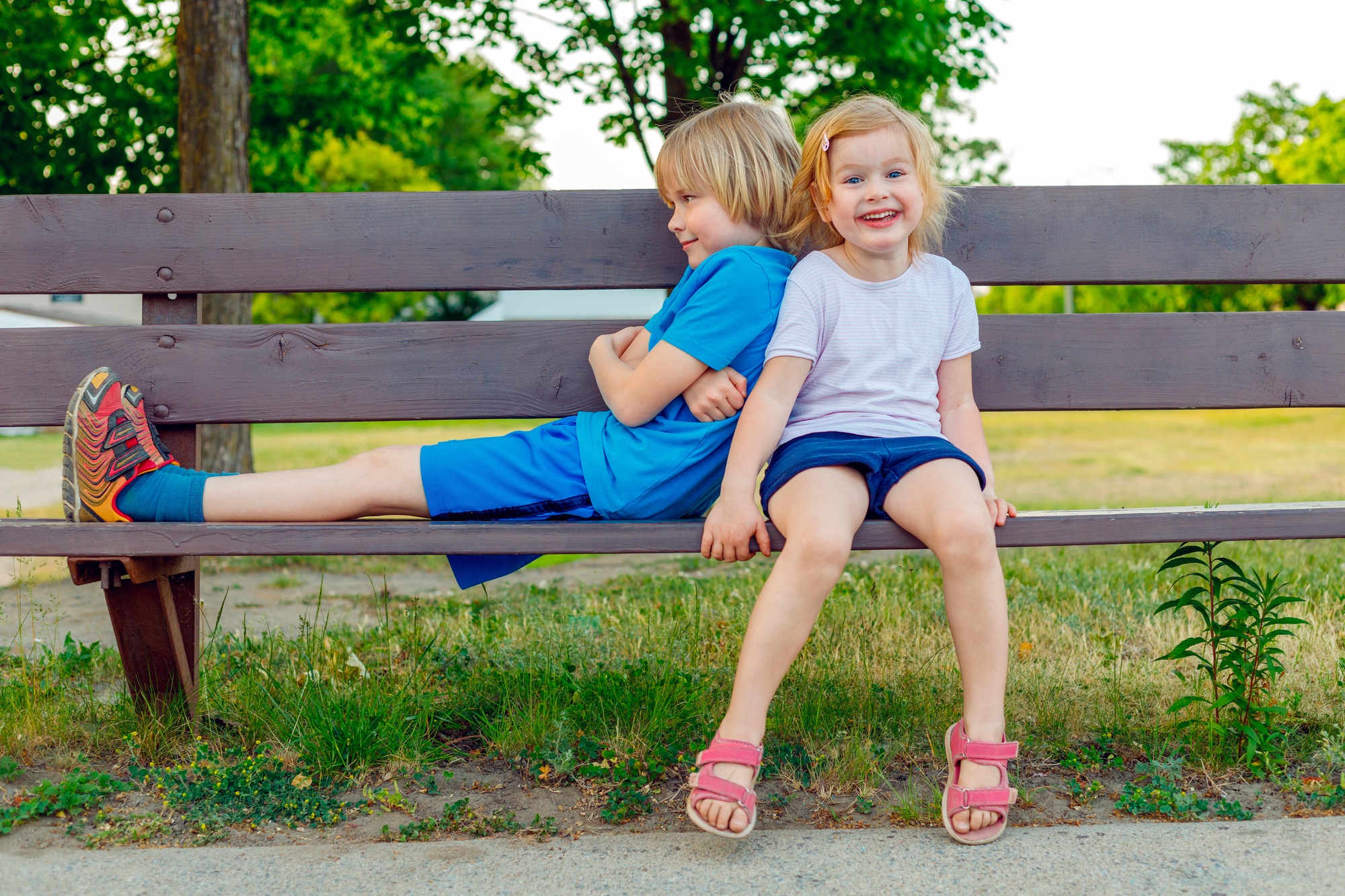 Children sitting on bench in park. Smiling happy kids playing outside. Brother and sister having fun