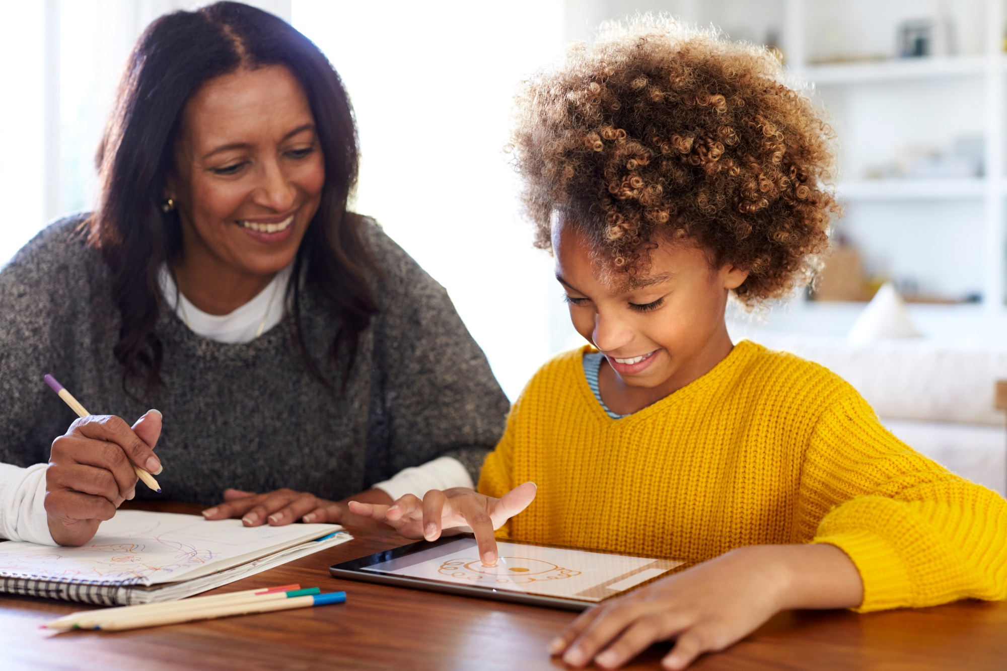 Mixed race young grandmother sitting at table with granddaughter using a tablet computer