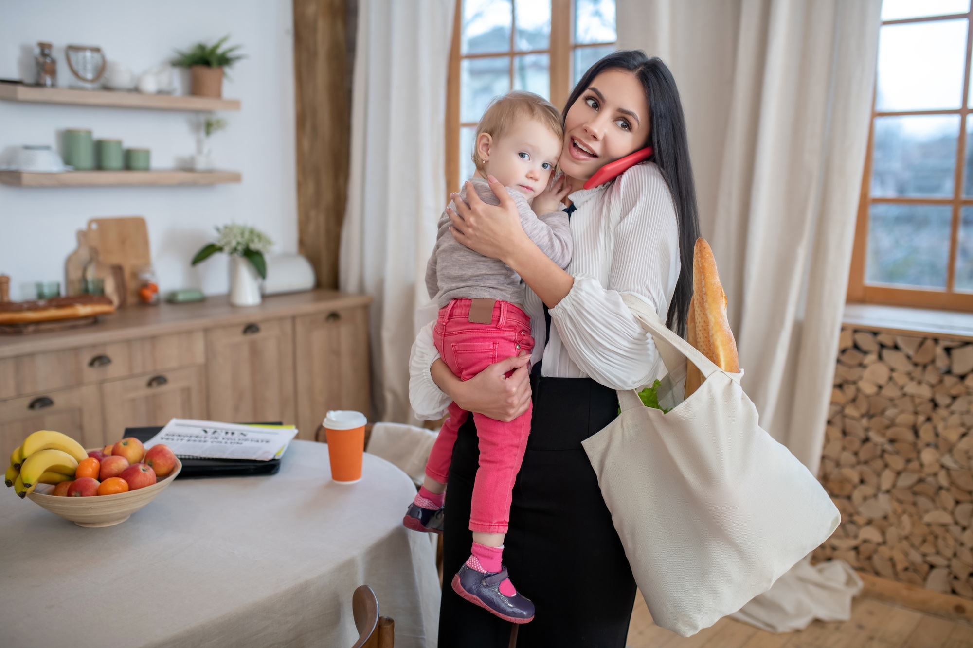 Mom holding daughter and shopping bag, talking on the phone